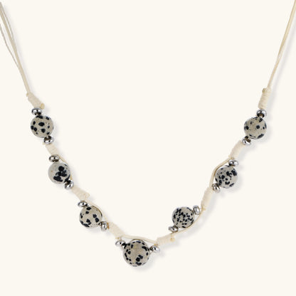 Adjustable cream cord necklace with white spotted stone beads featuring black speckles on neutral background