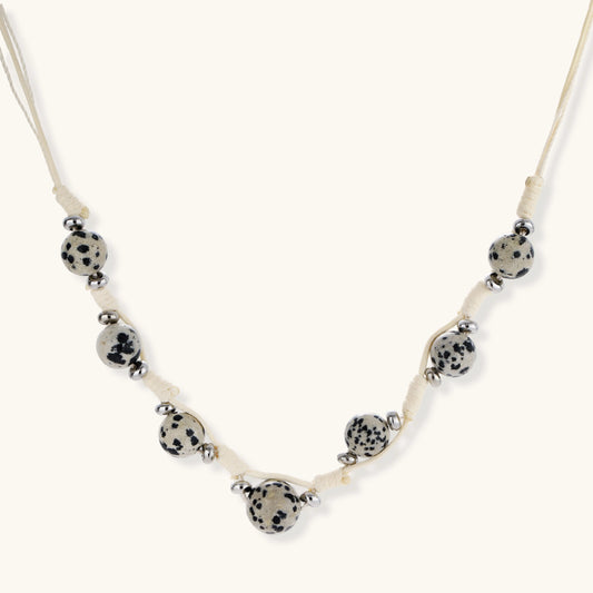 Adjustable cream cord necklace with white spotted stone beads featuring black speckles on neutral background