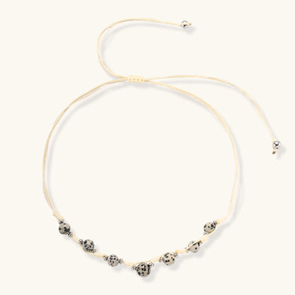 Adjustable cream cord necklace with white spotted stone beads featuring black speckles on neutral background
