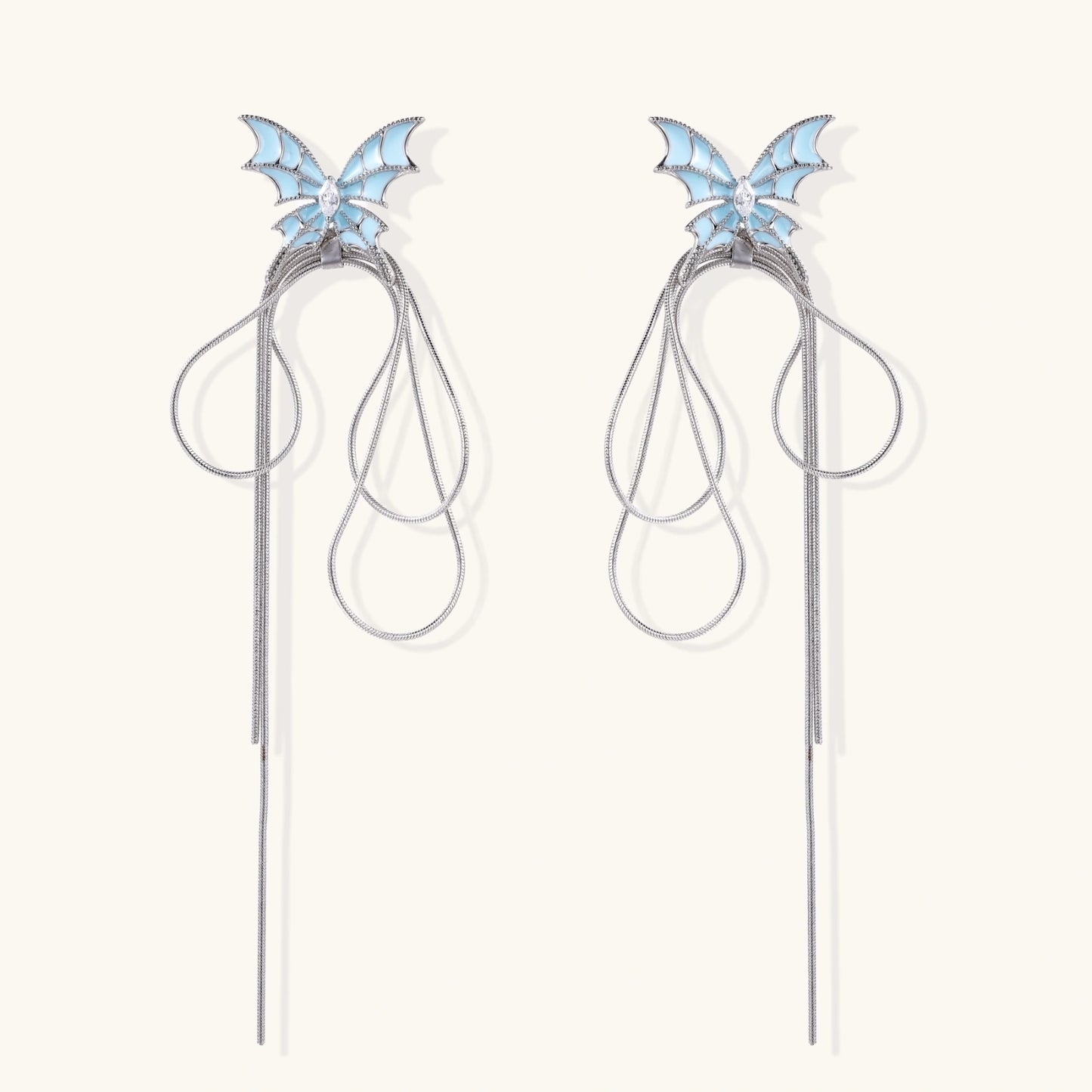 Long silver-tone earrings with powder blue enamel butterfly studs and flowing chain tassels on cream background