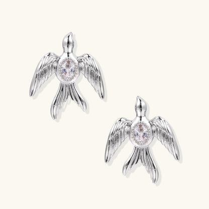 White gold-plated bird earrings with spread wings and oval zirconia center on cream background