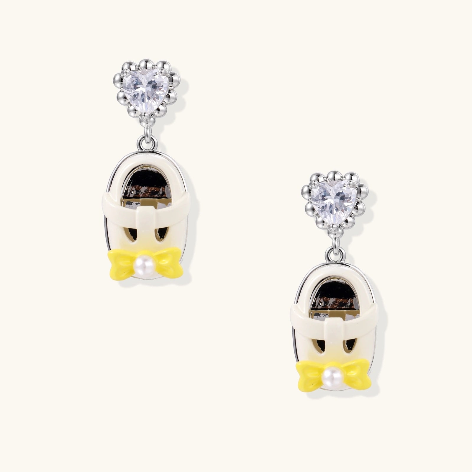 Dangle earrings with heart-shaped zirconia tops and white penguin charms with yellow bow ties on white gold plated setting.