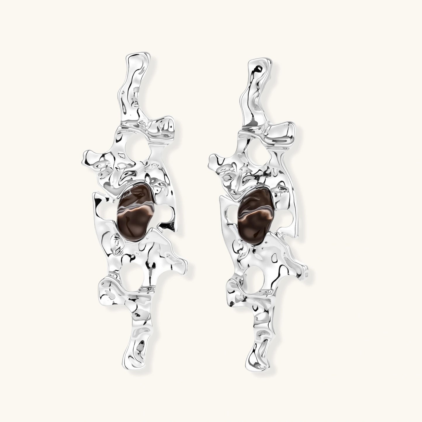 Flowing silver-toned earrings with organic liquid shapes and embedded brown resin stones on white background.