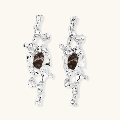 Flowing silver-toned earrings with organic liquid shapes and embedded brown resin stones on white background.