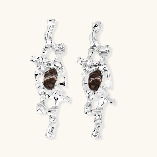 Flowing silver-toned earrings with organic liquid shapes and embedded brown resin stones on white background.