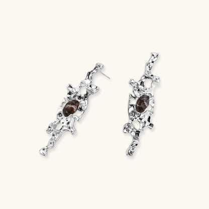 Flowing silver-toned earrings with organic liquid shapes and embedded brown resin stones on white background.