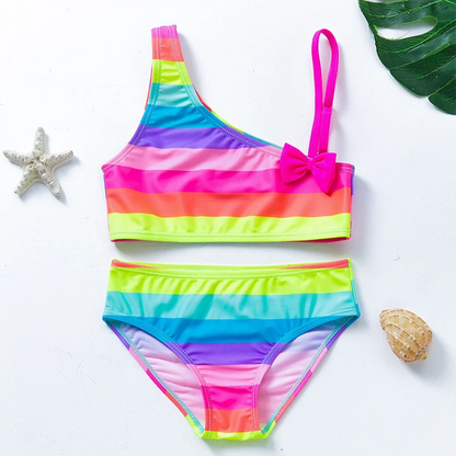 Two-piece rainbow striped girl's swimsuit featuring a golden crown 'Queen' graphic and a pink decorative bow.