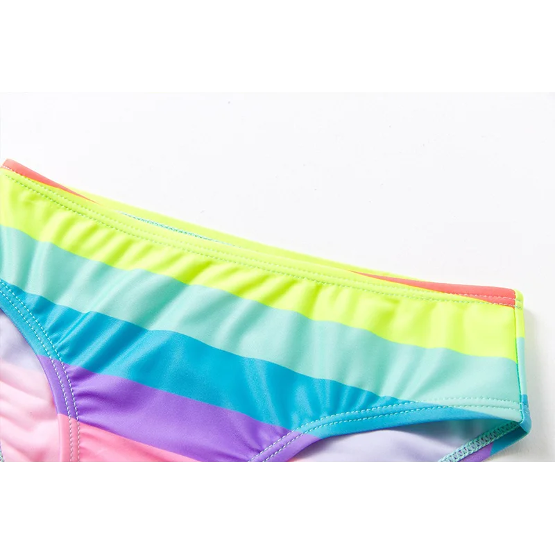 Two-piece rainbow striped girl's swimsuit featuring a golden crown 'Queen' graphic and a pink decorative bow.
