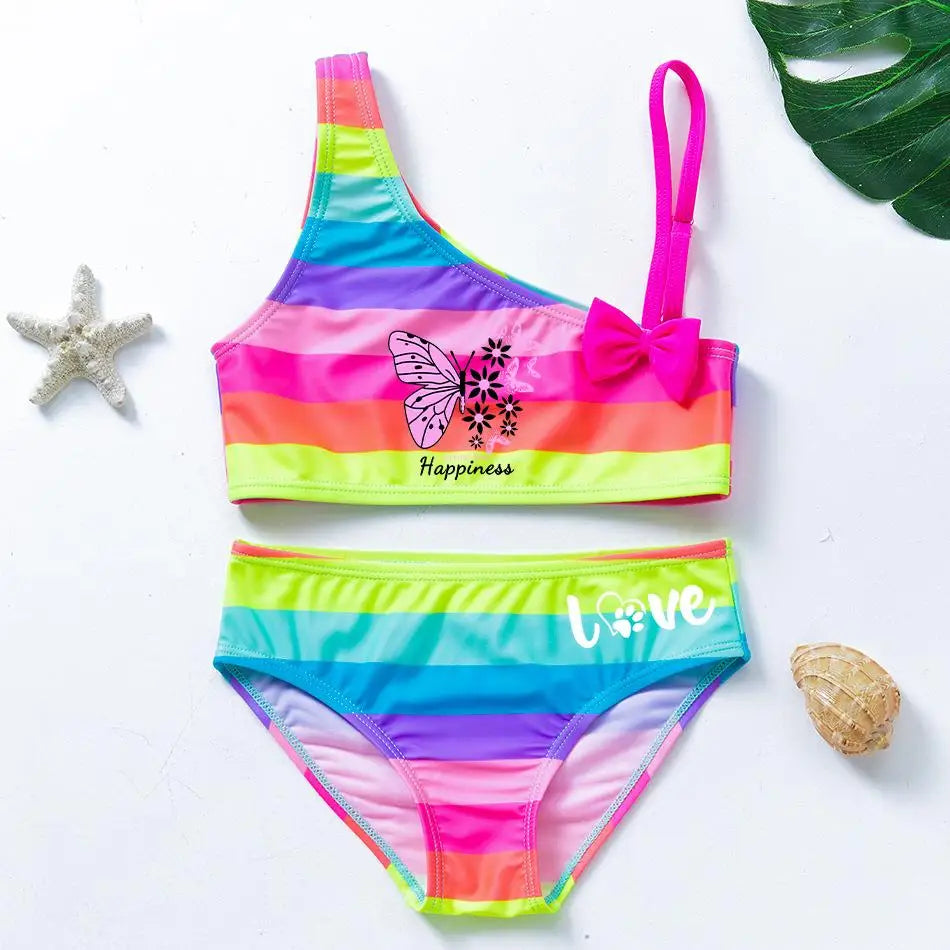Two-piece rainbow striped girl's swimsuit featuring a golden crown 'Queen' graphic and a pink decorative bow.