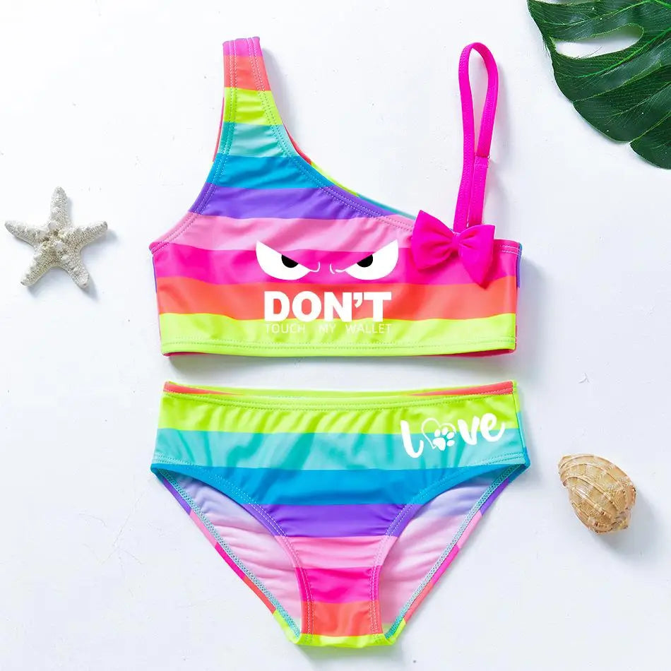 Two-piece rainbow striped girl's swimsuit featuring a golden crown 'Queen' graphic and a pink decorative bow.