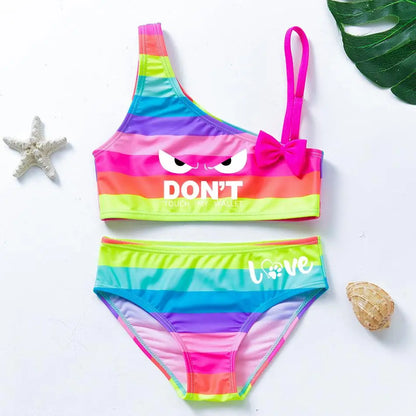 Two-piece rainbow striped girl's swimsuit featuring a golden crown 'Queen' graphic and a pink decorative bow.