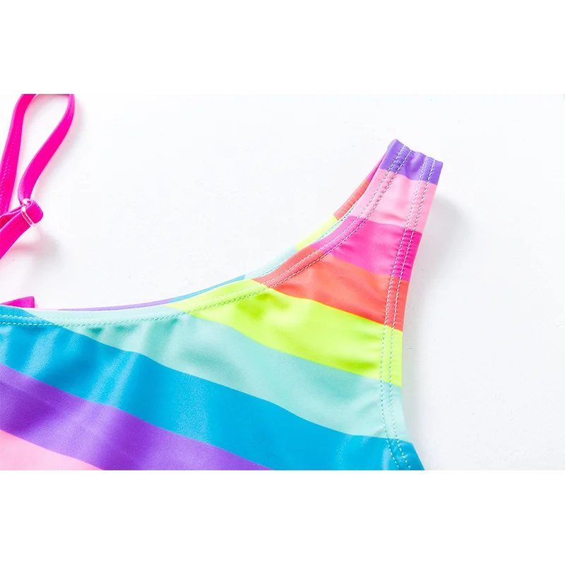 Two-piece rainbow striped girl's swimsuit featuring a golden crown 'Queen' graphic and a pink decorative bow.