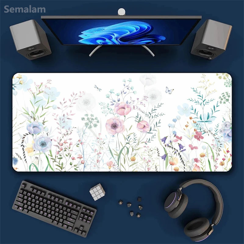 Top view of a large floral mouse pad with a complete computer setup on a blue background.