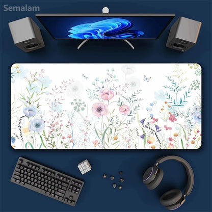 Top view of a large floral mouse pad with a complete computer setup on a blue background.