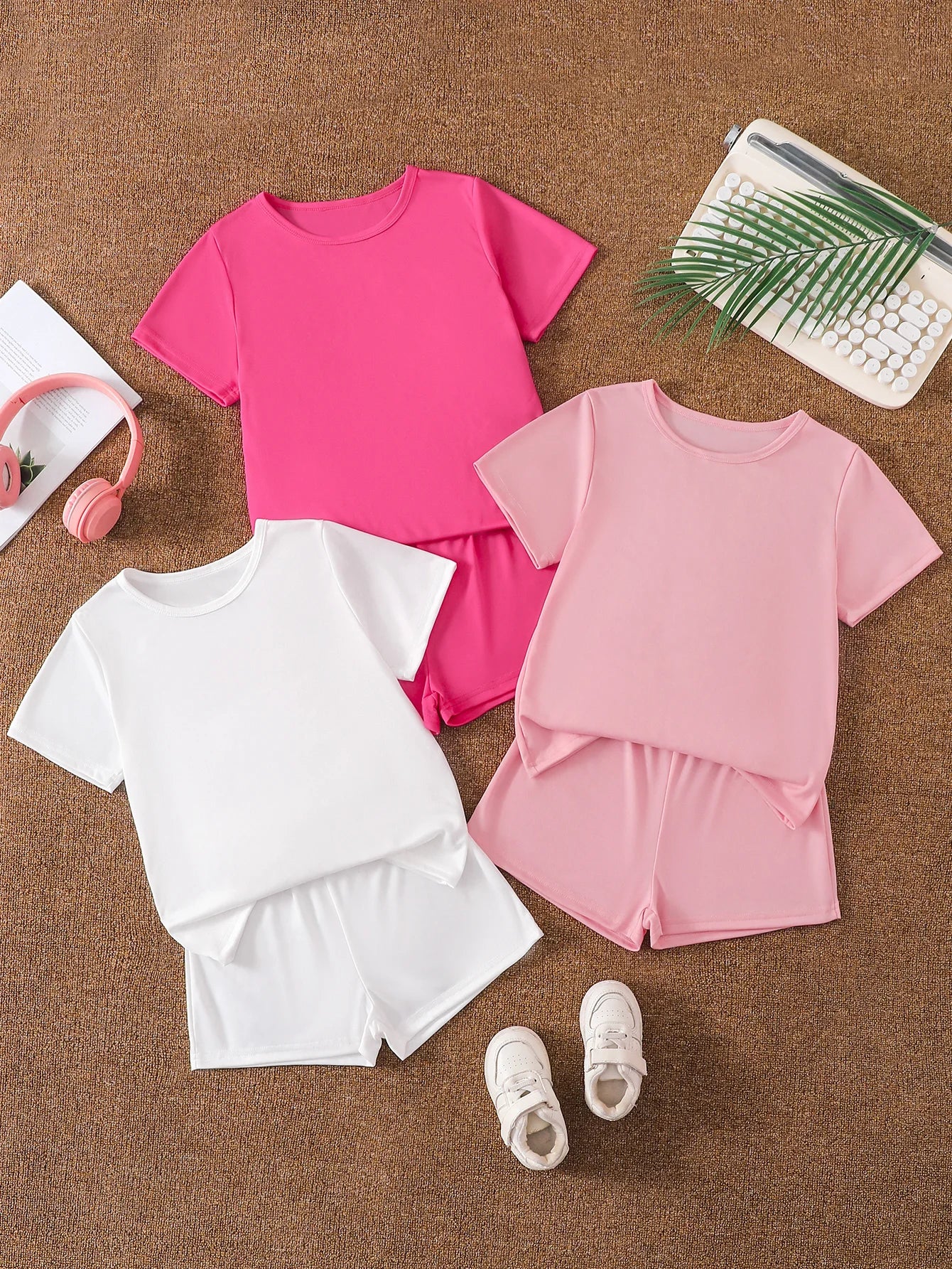 Flatlay of three girls' 2-piece solid color sets in white, light pink, and hot pink.