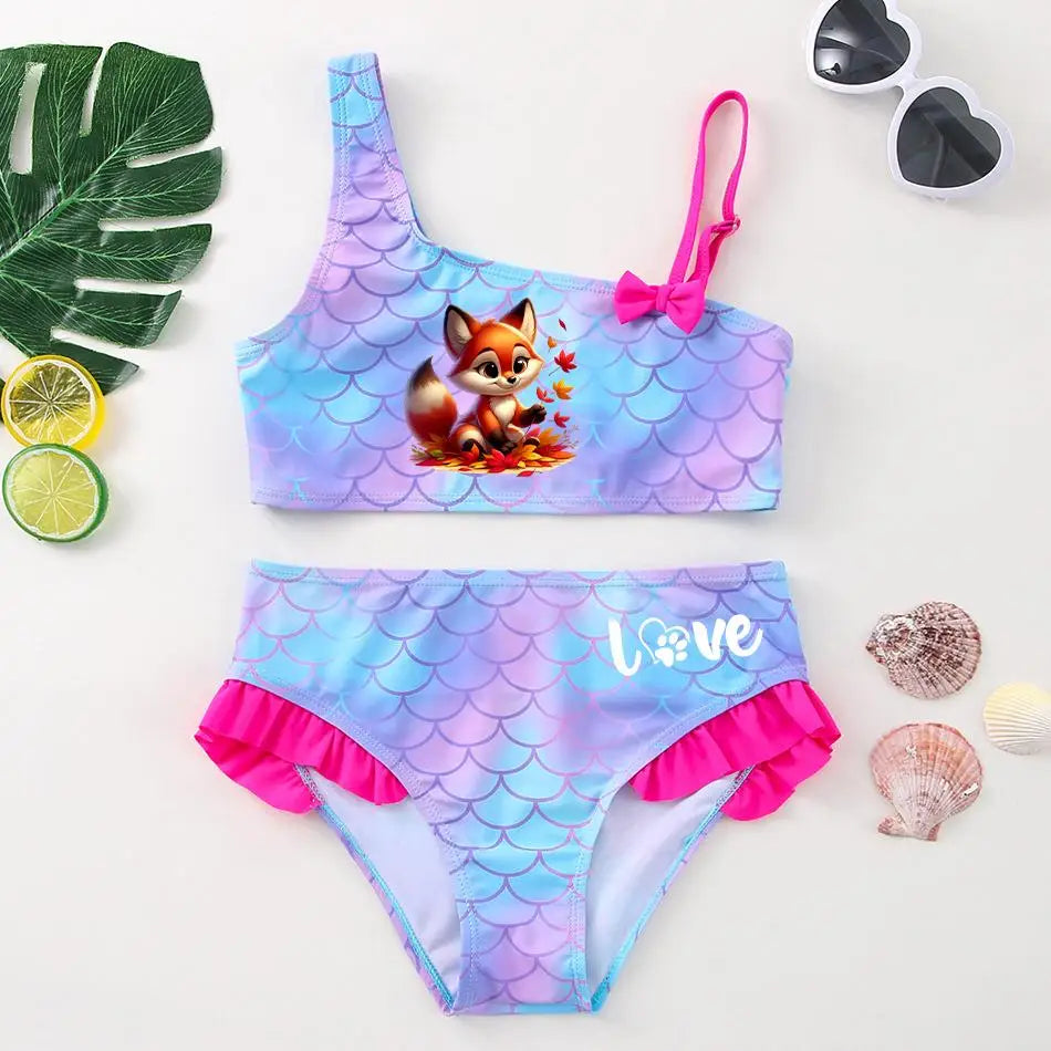 Two-piece girl's bikini featuring a chibi fox graphic, lavender mermaid scale pattern, and pink ruffles.