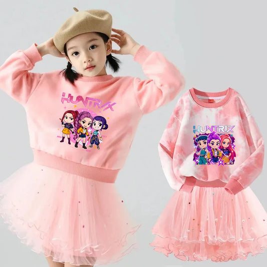 Young girl wearing a pink K-Pop HUNTRX sweatshirt and pearl-beaded tulle skirt, alongside a tie-dye version of the set.