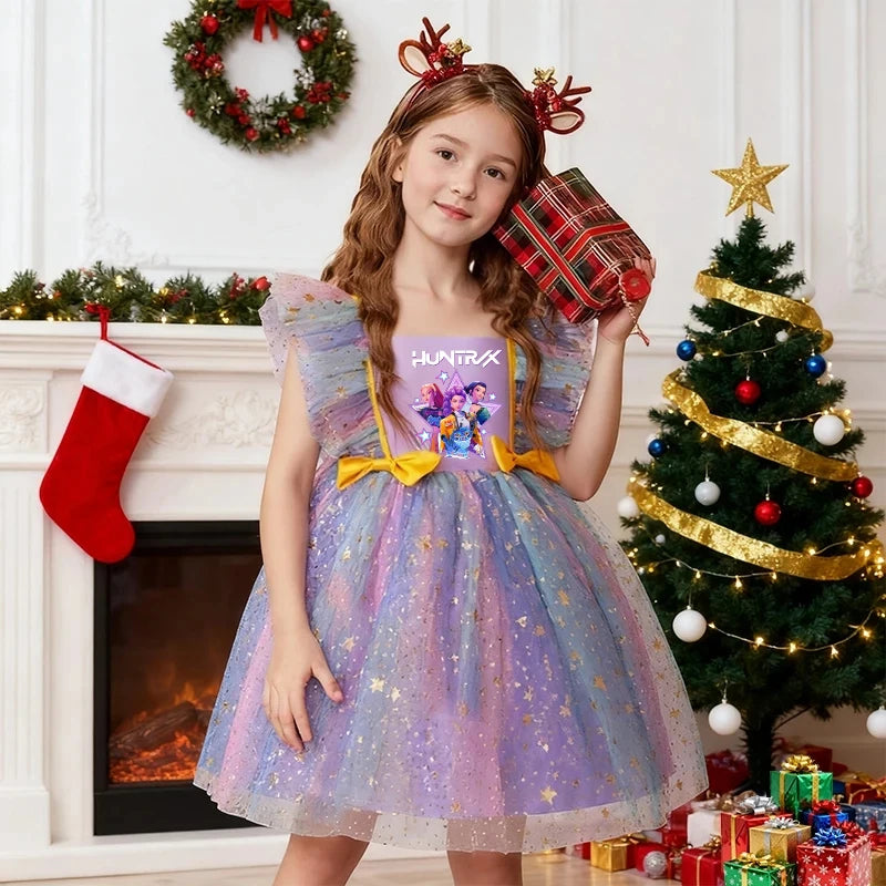 Young girl in a rainbow K-Pop HUNTRX dress with gold stars and reindeer antlers in front of a Christmas tree.