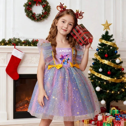 Young girl in a rainbow K-Pop HUNTRX dress with gold stars and reindeer antlers in front of a Christmas tree.