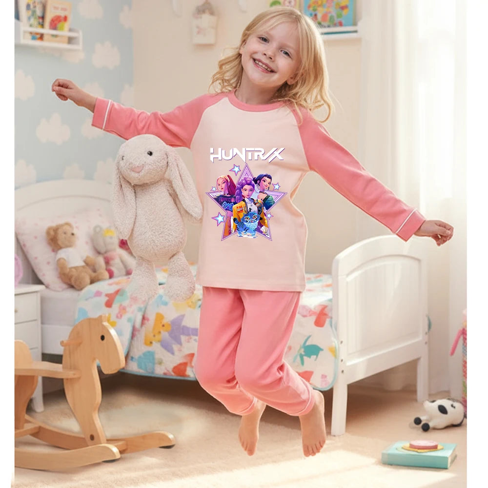 Young girl jumping on a bed wearing a pink and cream HUNTRX long-sleeve cotton pajama set.