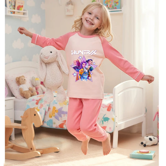 Young girl jumping on a bed wearing a pink and cream HUNTRX long-sleeve cotton pajama set.