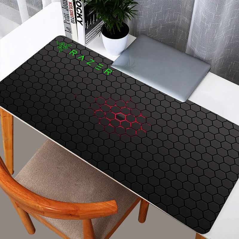Sleek black Razer hexagon pattern XXL gaming mouse pad on a white desk with a laptop.