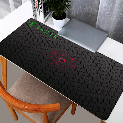 Sleek black Razer hexagon pattern XXL gaming mouse pad on a white desk with a laptop.