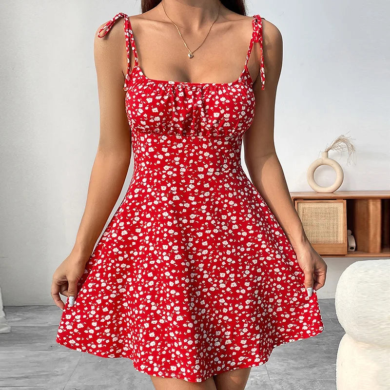 Woman wearing a red summer camisole mini dress with white floral print and adjustable bow shoulder straps.
