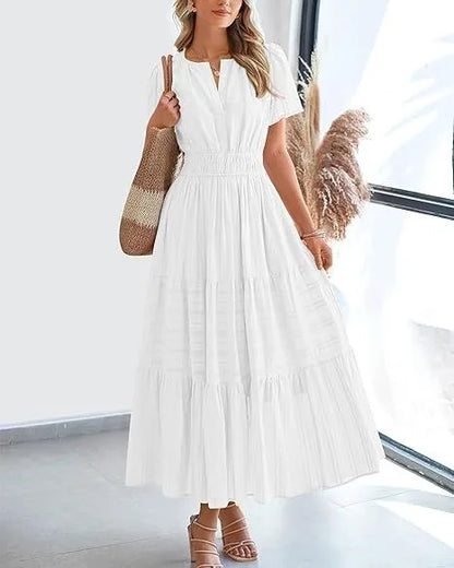 Woman wearing a white tiered boho midi dress with bubble sleeves and smocked waist standing in a bright room.